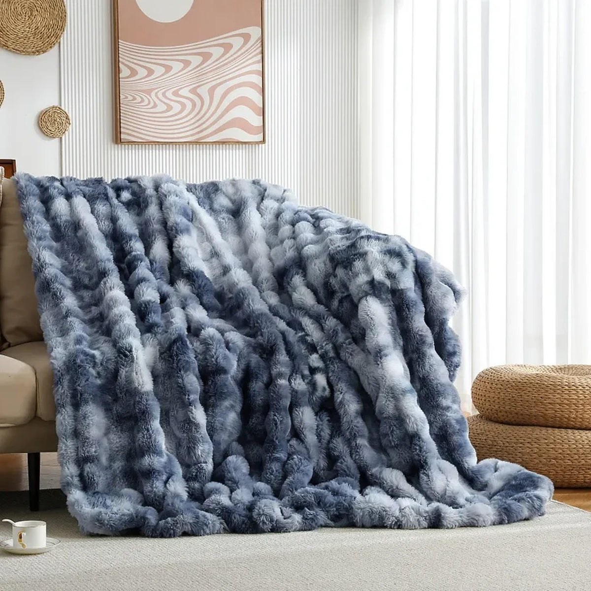 A plush faux-fur throw blanket in blue and white is draped over a beige sofa in a bright, modern living room with white curtains and wall art.
